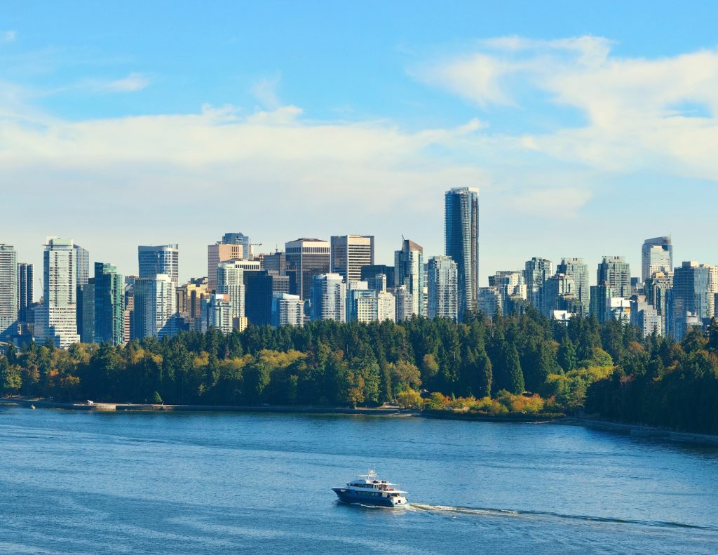 A boat floating on the ocean with the Vancouver skyline in the background under a clear sky.